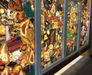 In the museum, the diversity of the mineral world is displayed in a floor-to-ceiling wall comprised of hundreds of illuminated translucent slabs of colorful minerals.
