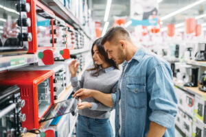 A young couple stand in a store aisle and look at a bright red toaster oven.