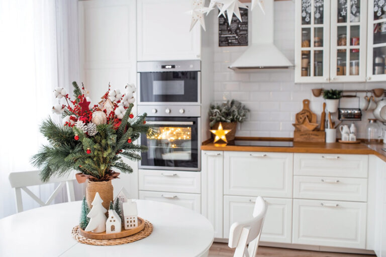 A spruce bouquet with red berries, toys, cotton on a white kitchen table. Christmas decorations in the interior. The concept of preparation for the New Year's holiday 2024.