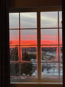 A red-orange sunset as seen through a window with mullins.