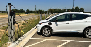 A white Chevy Bolt is plugged in to a level 2 charger