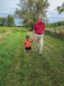 An elderly man and a small girl walk hand in hand by a corn field