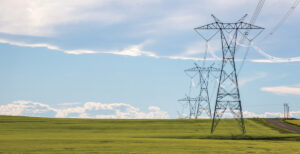 Power lines in a farm field on a sunny day with clouds