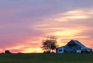 A large white barn is almost in silhouette at sundown