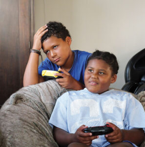 Two children are playing a video game. The boy appears to have lost and the girl is smiling while holding a wireless controller