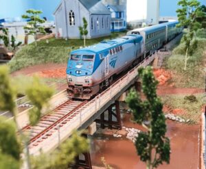 The blue and grey of a model Amtrak train crossing a miniature bridge