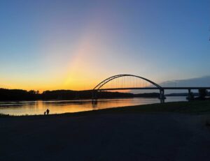 Silhouette of a bridge over a river. A parent walks a child along the riverbank