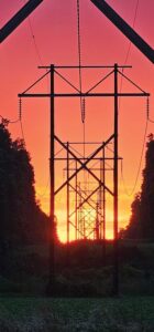 Silhouette of transmission power lines backlit by an orange and yellow sunset
