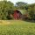Tucked into trees, a dilapidated red barn with a green roof can be seen