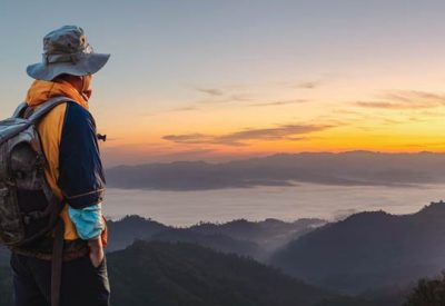 Hipster male hiker with backpack enjoying sunset on peak of foggy mountain. Tourist traveler on background view mockup.  Panoramic