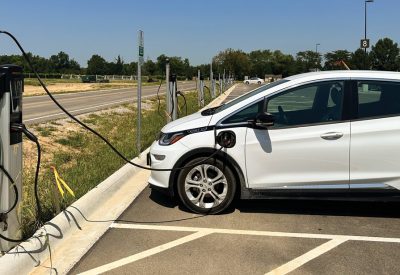 A white Chevy Bolt is plugged in to a level 2 charger