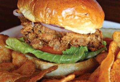 Large fried chicken sandwich on white plate with fries.