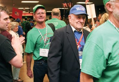 Craig Costello (center), a volunteer for the Land of Lincoln Honor Flight, agrees with Will Rogers who said, “We can’t all be heroes. Some of us have to stand on the curb and clap as they go by.”