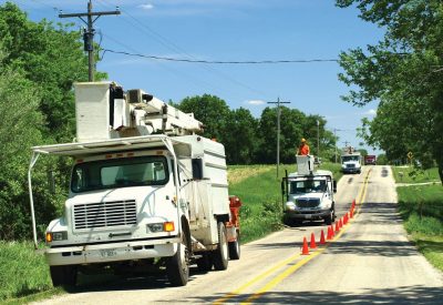 Three bucket trucks on a road with orange safety cones along the center line.