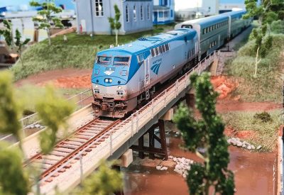 The blue and grey of a model Amtrak train crossing a miniature bridge