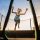 Child girl jumping high on big trampoline outside in garden on summer sunset.