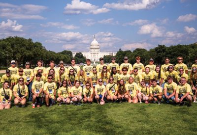 A large group of high school students pose in their yellow Youth Tour shirts in DC