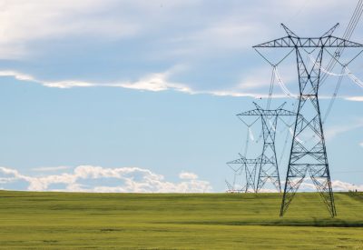 Power lines in a farm field on a sunny day with clouds
